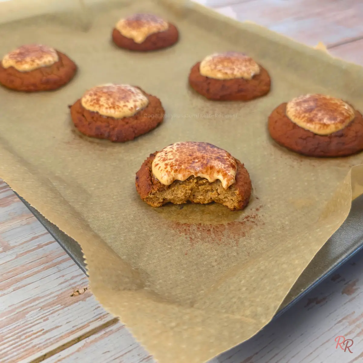 Soft keto cottage cheese tiramisu cookies cooling on a parchment-lined tray, with one cookie bitten to show the tender espresso-flavored center and mousse topping.