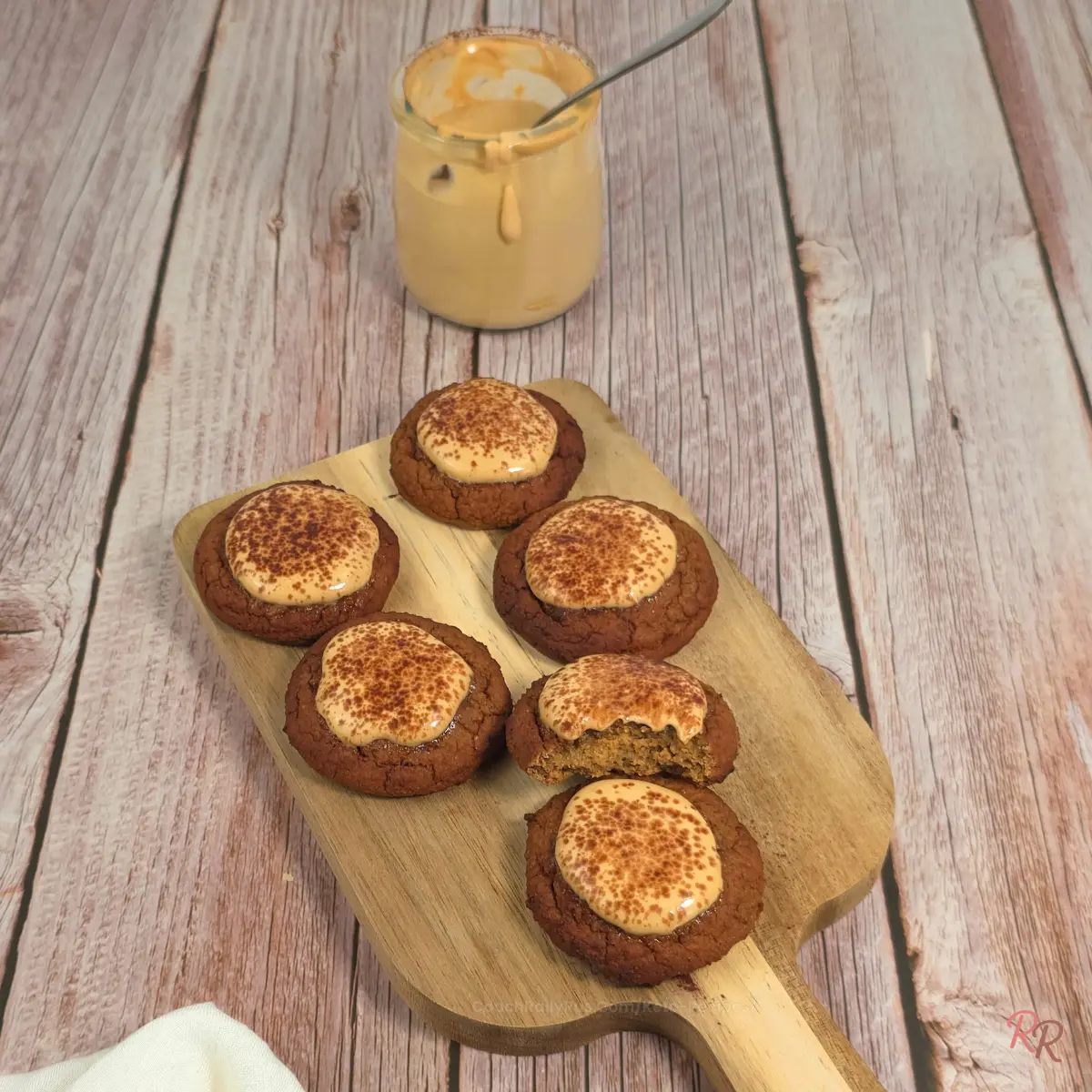 Tray of keto cottage cheese tiramisu cookies topped with mousse, with a jar of mousse behind them on a wood surface.