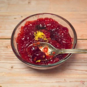 Sugar free keto cranberry sauce in a glass bowl with lemon zest on top, cottage-core wooden background, bright red texture.