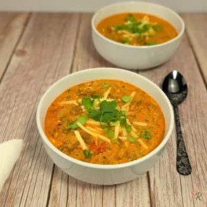 Close-up of keto cottage cheese taco soup with ground beef, topped with shredded cheese and cilantro, served in white bowls on rustic wood.