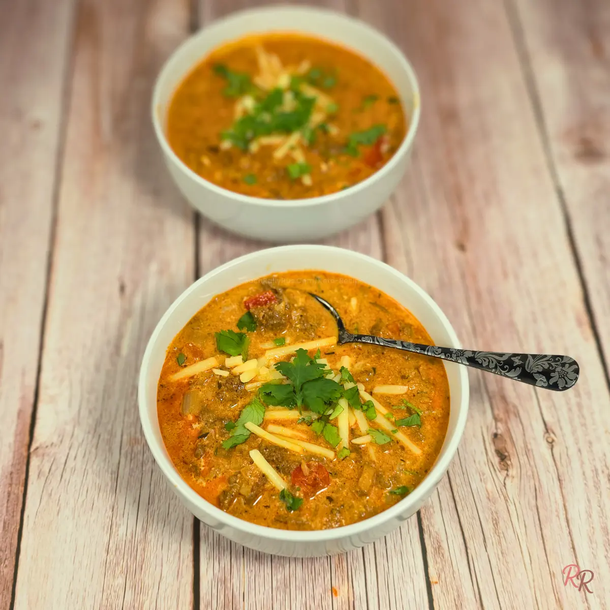 Keto Cottage Cheese Taco Soup with Cilantro Two bowls of cheesy keto taco soup topped with cilantro and served on a wood background.