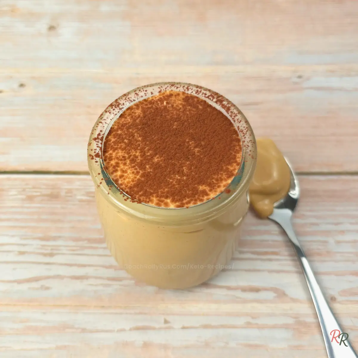 Keto cottage cheese tiramisu mousse in a glass jar topped with cocoa powder, with a spoonful of mousse resting beside it.