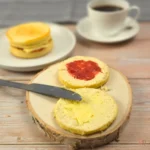 Keto cottage cheese English muffins with butter and sugar free jam on a wood slice, coffee in the background