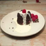 High protein keto chocolate raspberry cottage cheese mug cake topped with cream and a fresh raspberry on a white plate