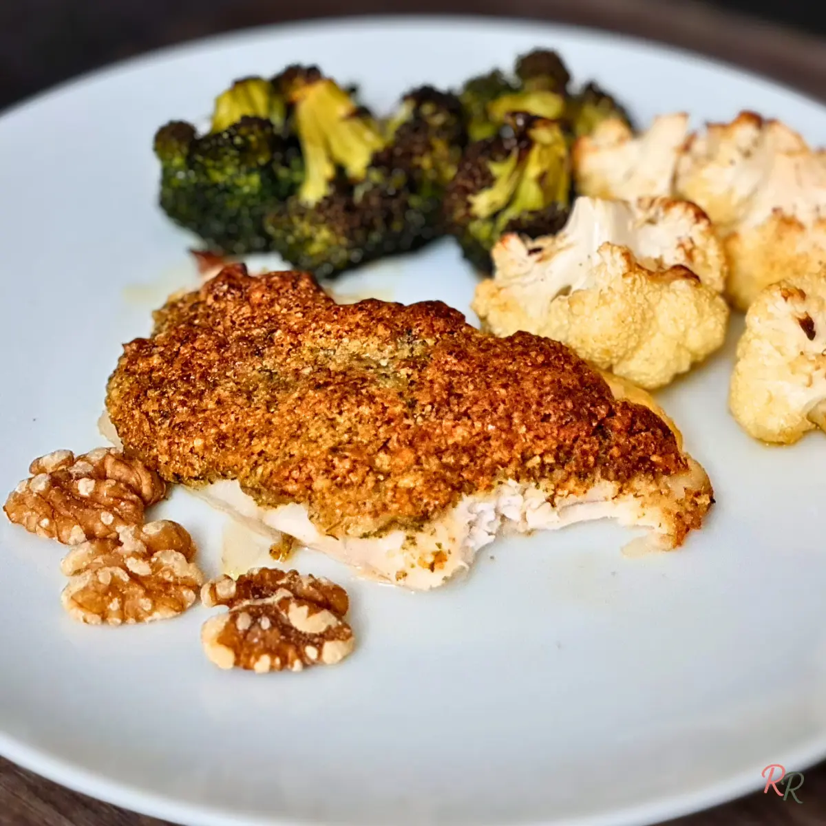 Walnut-crusted baked cod with roasted broccoli and cauliflower on a white plate.