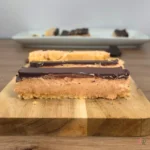 Close-up of a layered cottage cheese peanut butter freezer bar with a chocolate top and almond flour crust on a cutting board.