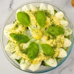 Glass bowl of keto egg salad without mayo topped with sliced eggs, creamy yolk dressing, fresh basil leaves, and dill