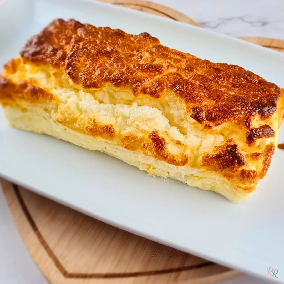 Whole loaf of cottage cheese and egg bread with a golden cracked crust on a white plate set on a wooden board