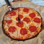 Sliced cottage cheese pepperoni pizza on parchment with one slice being lifted by a knife