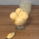 Salted caramel cottage cheese ice cream in smooth scoops in a small glass dish, Ninja Creami pint in the background, spoon with melty ice cream in front