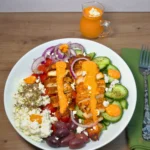 Gyro chicken Greek salad bowl topped with creamy red cottage cheese dressing, a jug of the dressing beside it