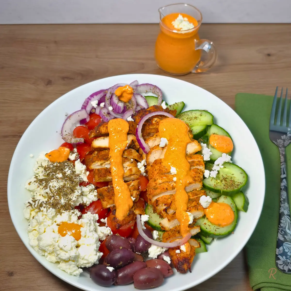 Gyro chicken Greek salad bowl topped with creamy red cottage cheese dressing, a jug of the dressing beside it