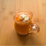 Roasted red pepper feta cottage cheese dressing in a small glass pitcher on a wooden board, topped with crumbled feta